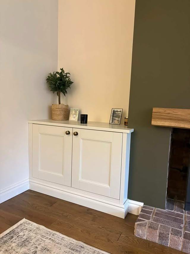 Fitted cream cabinet with brass knobs beside a fireplace